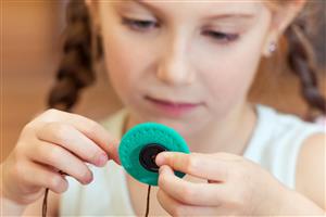 Child sewing a button onto a piece of felt with a blunt needle.