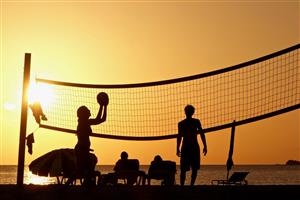 Silhouette of a beach volleyball game in the amber light of sunset over the ocean